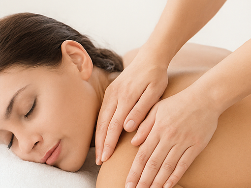 Une femme reçoit un massage sur le dos, les yeux fermés, avec une main posée délicatement sur son épaule.